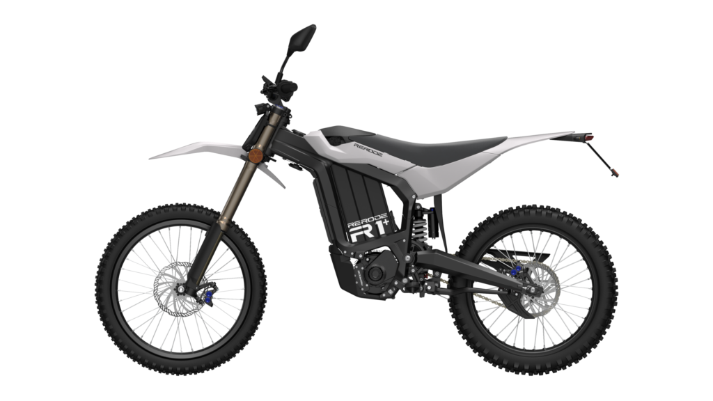 A side view of the RE RODE R1+ electric enduro motorcycle. Clearly visible against a deep black studio background are the black frame with white fairing, the distinctive front fork, the rugged knobby tires, the chain drive, and the central shock absorber.